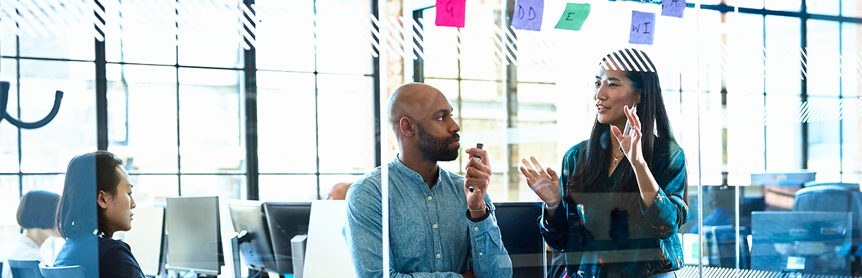 Femme d'affaires en jeans et chemise, debout face à un homme, et discutant d'idées lors d'une séance de brainstorming